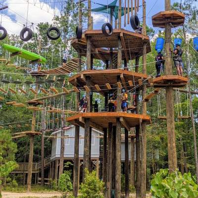 People navigating an elevated rope course with wooden platforms and various suspended obstacles, surrounded by trees.