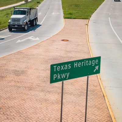 Road sign directing towards Texas Heritage Parkway with a truck on the adjacent road.