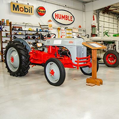 A vintage tractor is displayed in a museum with vintage Mobil, Gulf, and Humble signs on the walls.